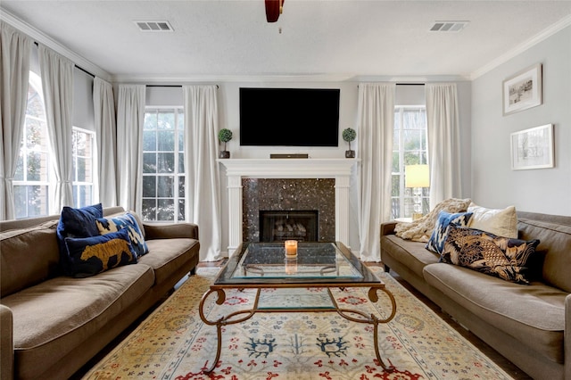 living room featuring a textured ceiling, ornamental molding, a premium fireplace, and ceiling fan