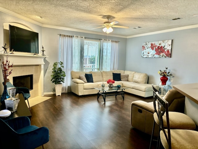 living room featuring crown molding, a tile fireplace, ceiling fan, a textured ceiling, and dark hardwood / wood-style flooring