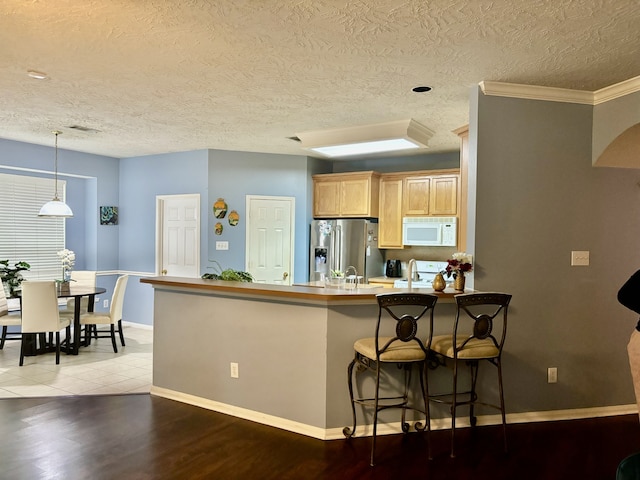 kitchen with a breakfast bar, stainless steel refrigerator with ice dispenser, light brown cabinetry, decorative light fixtures, and kitchen peninsula