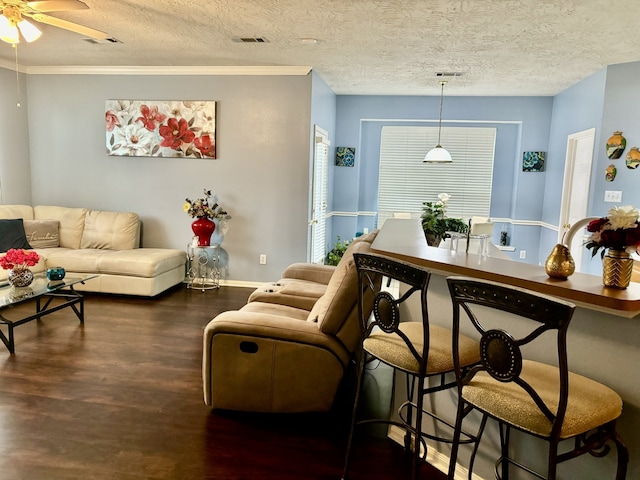 living room with crown molding, dark wood-type flooring, ceiling fan, and a textured ceiling