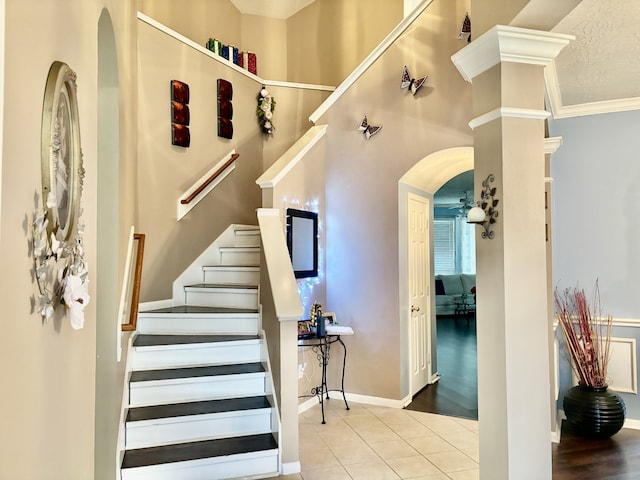 stairs with decorative columns, tile patterned flooring, ornamental molding, ceiling fan, and a textured ceiling