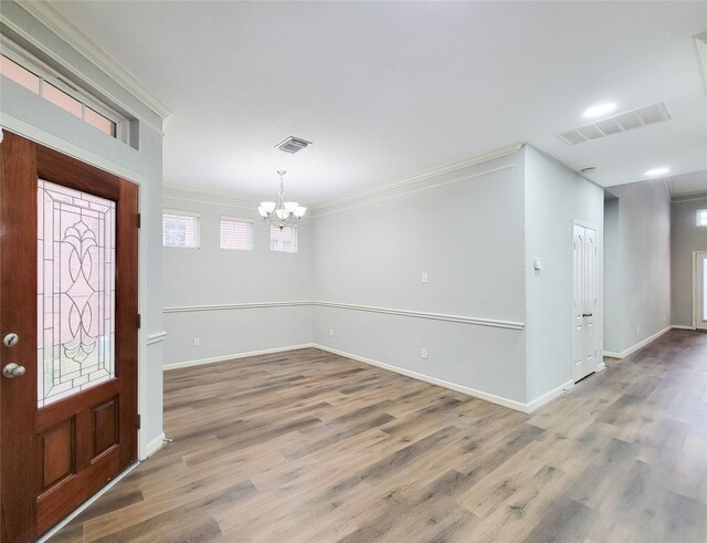 entrance foyer with ornamental molding, wood-type flooring, and a chandelier