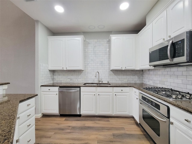 kitchen featuring dark stone countertops, appliances with stainless steel finishes, white cabinets, and a sink