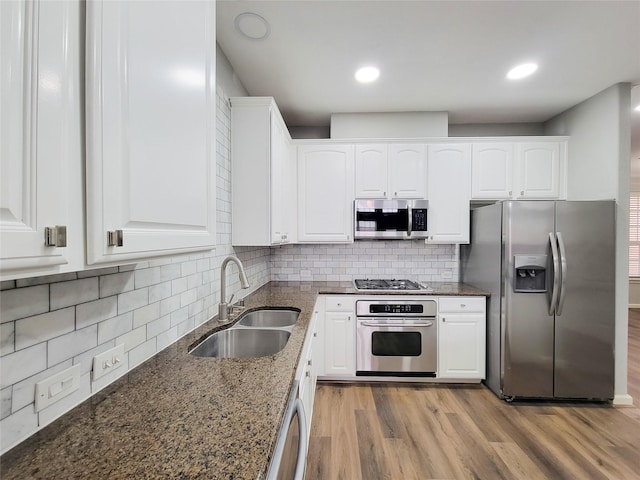 kitchen featuring white cabinets, dark stone counters, stainless steel appliances, light wood-style floors, and a sink