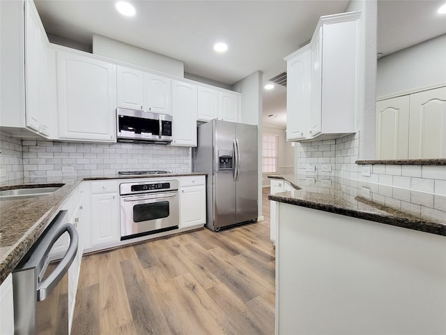 kitchen with tasteful backsplash, light hardwood / wood-style flooring, appliances with stainless steel finishes, dark stone counters, and white cabinets