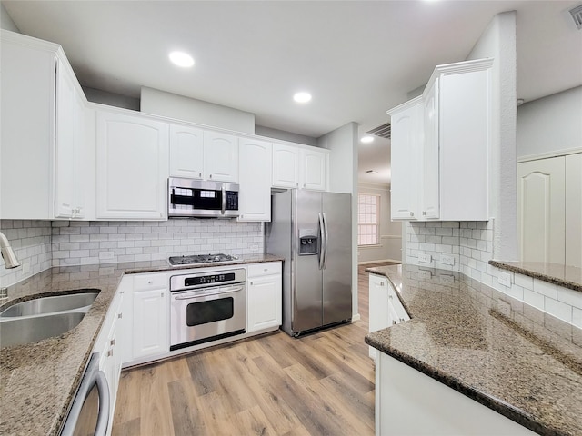 kitchen featuring sink, light hardwood / wood-style flooring, appliances with stainless steel finishes, white cabinetry, and dark stone countertops