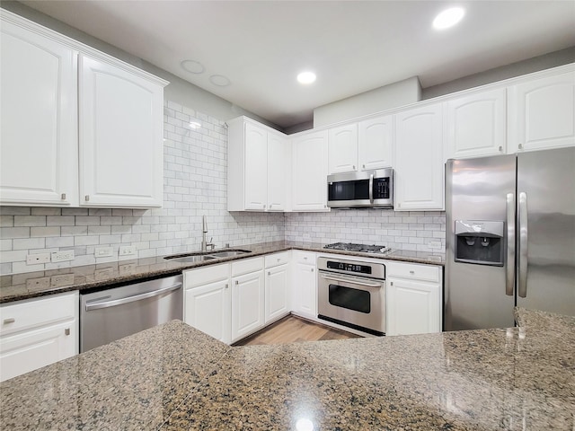 kitchen featuring white cabinets, appliances with stainless steel finishes, backsplash, dark stone countertops, and a sink