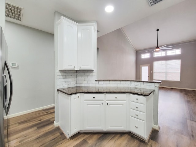 kitchen with dark hardwood / wood-style floors, stainless steel fridge, kitchen peninsula, decorative backsplash, and white cabinets