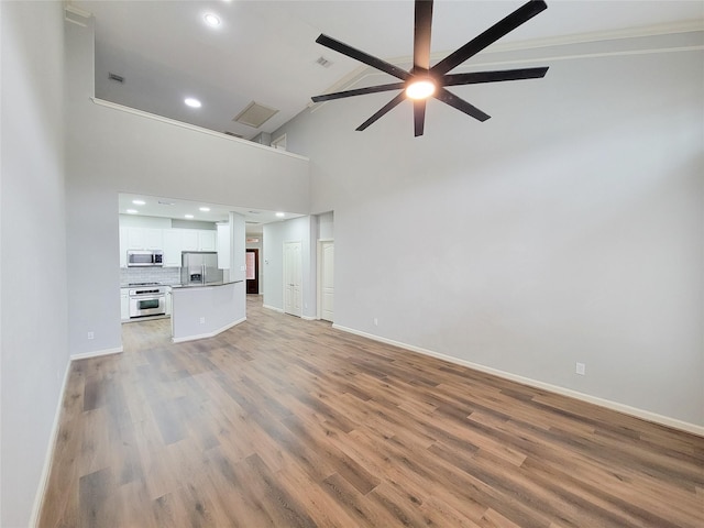 unfurnished living room featuring visible vents, a towering ceiling, a ceiling fan, wood finished floors, and baseboards