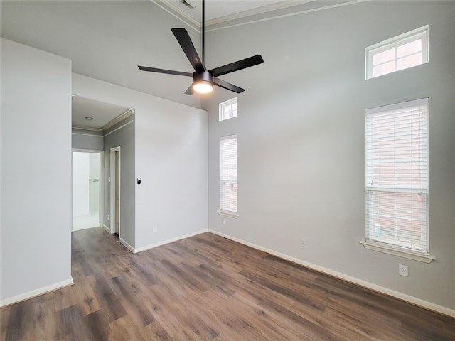 unfurnished room with a towering ceiling, ornamental molding, ceiling fan, wood finished floors, and baseboards