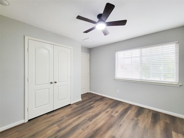 unfurnished bedroom featuring dark wood-style floors, a closet, visible vents, a ceiling fan, and baseboards