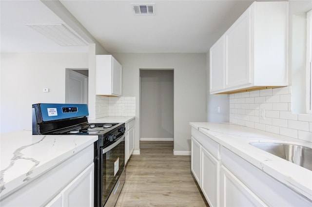 kitchen featuring light stone counters, stainless steel gas range oven, light hardwood / wood-style floors, and white cabinets