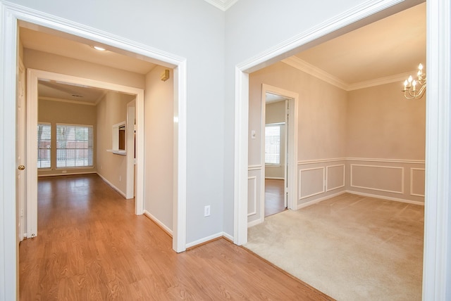 hall with crown molding, light hardwood / wood-style floors, and an inviting chandelier