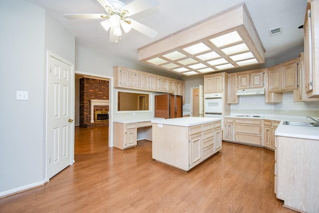 kitchen featuring sink, tasteful backsplash, a center island, light wood-type flooring, and white appliances