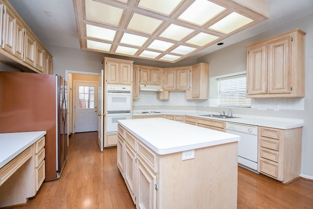 kitchen with light brown cabinetry, sink, light hardwood / wood-style flooring, a kitchen island, and white appliances