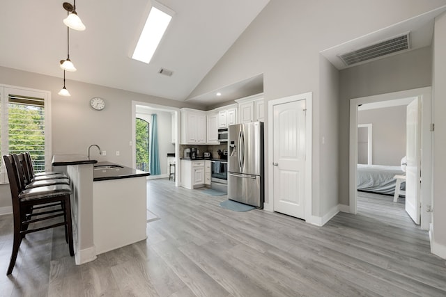 kitchen featuring pendant lighting, a breakfast bar area, appliances with stainless steel finishes, high vaulted ceiling, and white cabinets