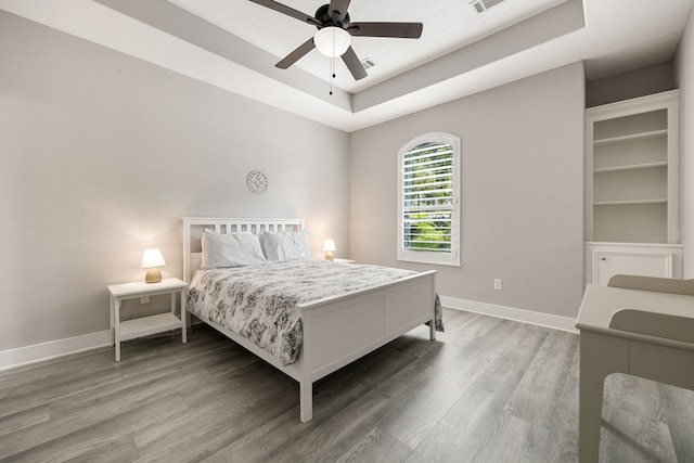 bedroom with hardwood / wood-style flooring, ceiling fan, and a raised ceiling