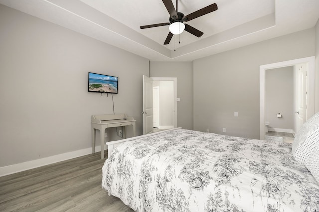 bedroom with hardwood / wood-style flooring, ensuite bath, ceiling fan, and a tray ceiling