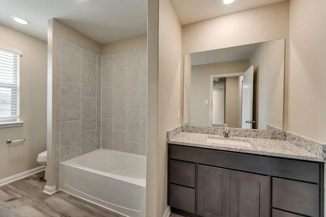 full bathroom with hardwood / wood-style flooring, vanity, tiled shower / bath, and toilet