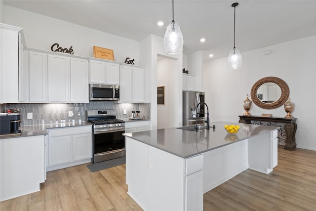 kitchen with white cabinetry, appliances with stainless steel finishes, pendant lighting, and a center island with sink