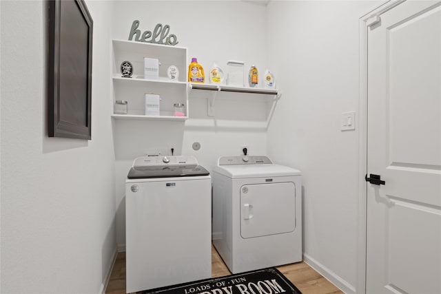 clothes washing area with washer and clothes dryer and light wood-type flooring