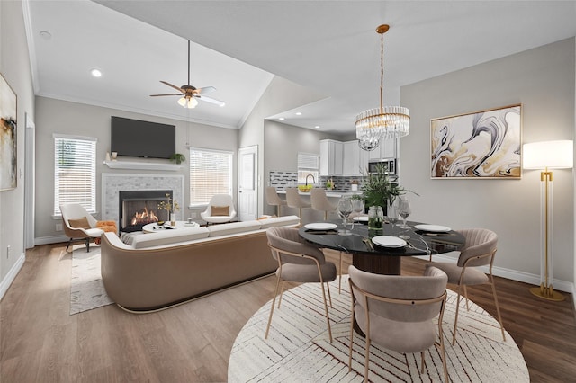 dining area with a tiled fireplace, vaulted ceiling, ceiling fan with notable chandelier, and light hardwood / wood-style floors