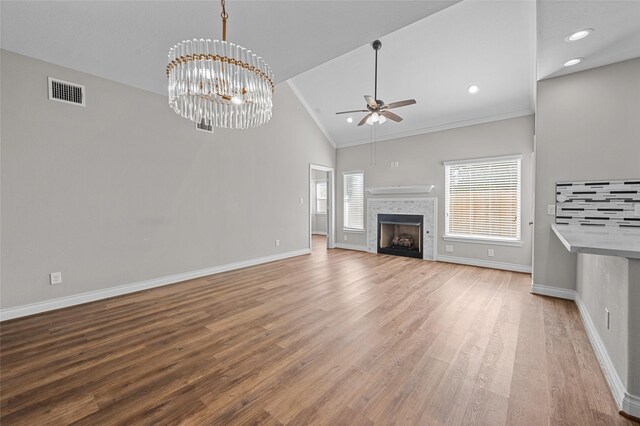 unfurnished living room with crown molding, hardwood / wood-style floors, high vaulted ceiling, a tiled fireplace, and ceiling fan with notable chandelier