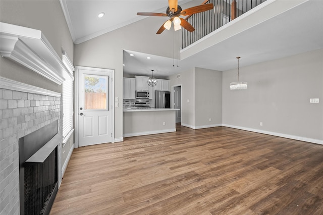 unfurnished living room featuring high vaulted ceiling, a fireplace, ornamental molding, ceiling fan with notable chandelier, and light wood-type flooring