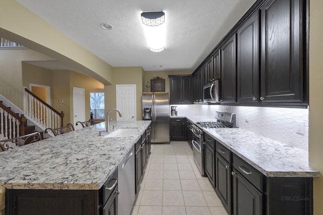 kitchen featuring appliances with stainless steel finishes, an island with sink, sink, backsplash, and light tile patterned floors