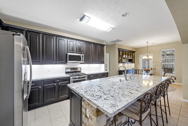 kitchen featuring light stone countertops, appliances with stainless steel finishes, a kitchen island with sink, and light tile patterned flooring