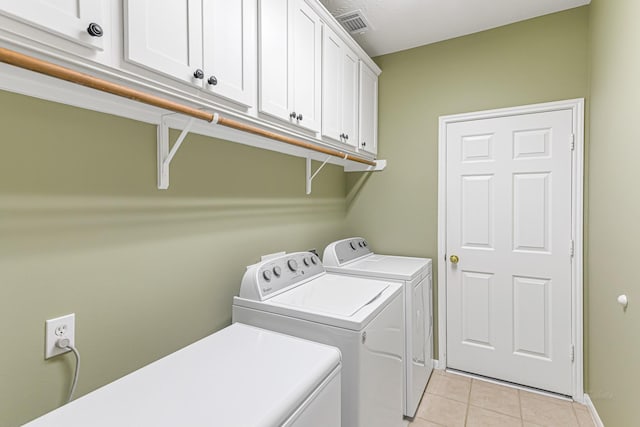 clothes washing area featuring cabinets, light tile patterned flooring, and washing machine and clothes dryer