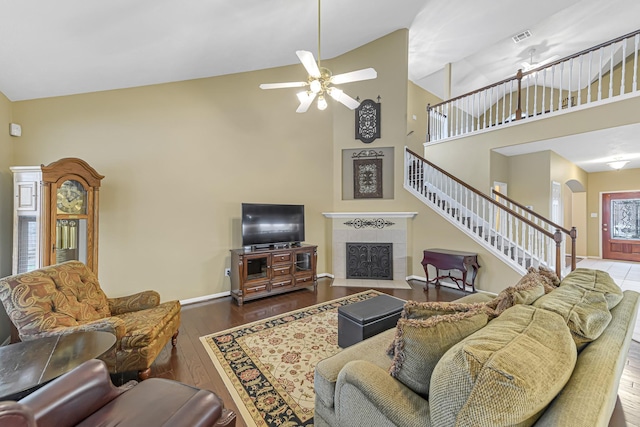 living room with a tiled fireplace, dark wood-type flooring, high vaulted ceiling, and ceiling fan