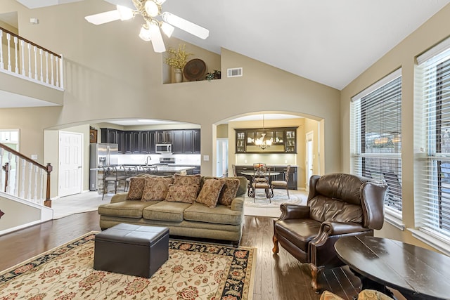 living room with sink, ceiling fan with notable chandelier, high vaulted ceiling, and light wood-type flooring