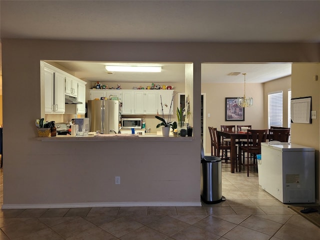 kitchen with decorative light fixtures, light tile patterned floors, appliances with stainless steel finishes, kitchen peninsula, and white cabinets