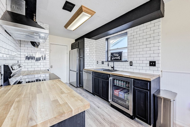 kitchen with wall chimney exhaust hood, sink, butcher block countertops, stainless steel appliances, and beverage cooler