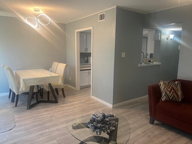 dining room featuring ornamental molding, a textured ceiling, a notable chandelier, and light wood-type flooring