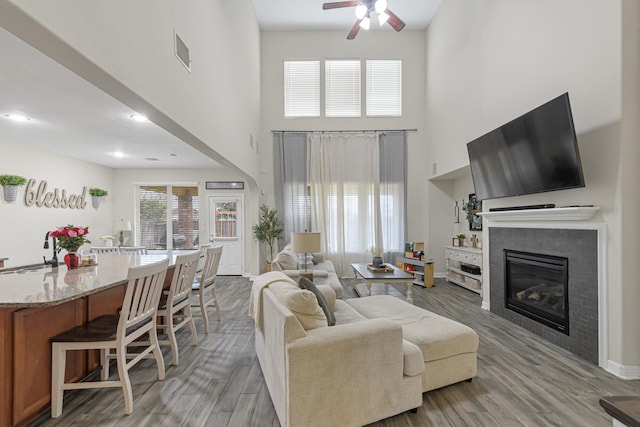 living room featuring hardwood / wood-style flooring, a fireplace, ceiling fan, and a high ceiling