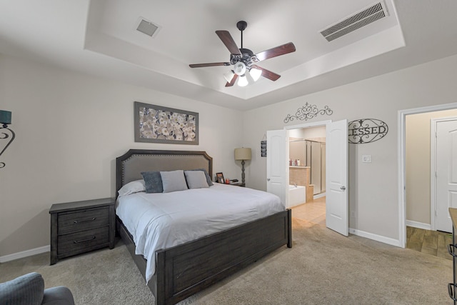 bedroom with light colored carpet, a raised ceiling, ceiling fan, and ensuite bathroom