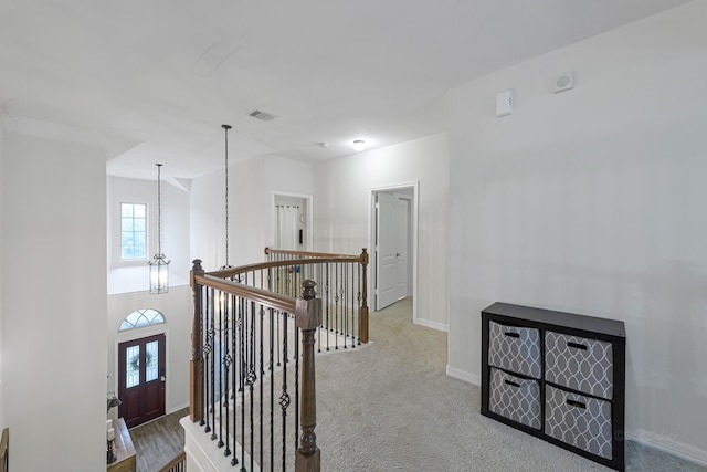 hallway with a notable chandelier and light colored carpet