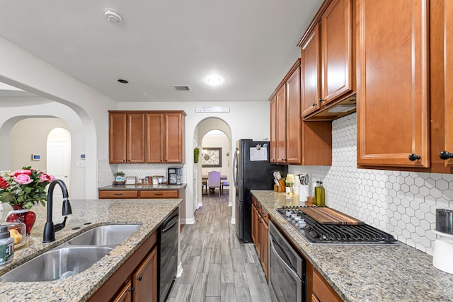 kitchen featuring sink, decorative backsplash, light stone counters, black appliances, and light wood-type flooring