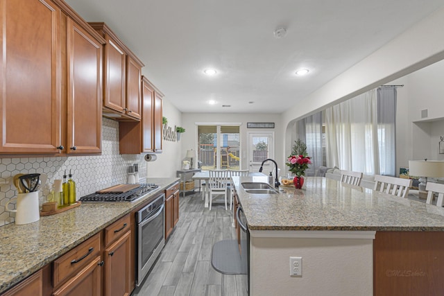 kitchen featuring sink, backsplash, stainless steel appliances, light hardwood / wood-style floors, and a center island with sink