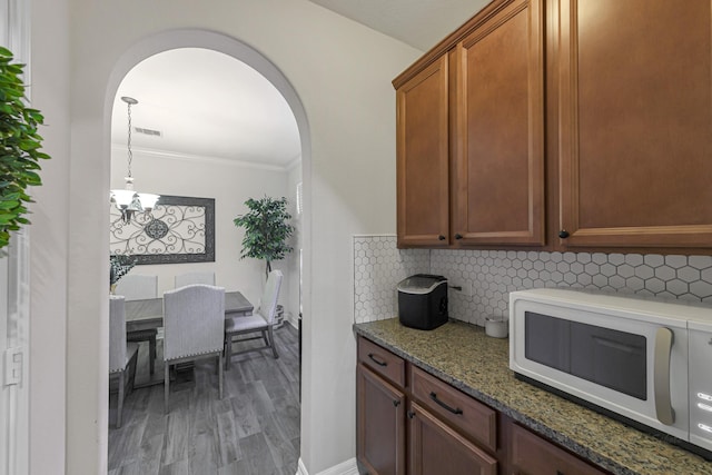 kitchen with dark stone countertops, backsplash, ornamental molding, and hardwood / wood-style floors