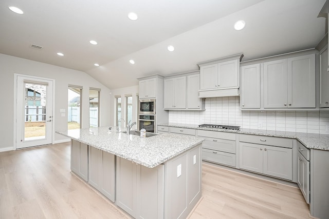 kitchen with tasteful backsplash, vaulted ceiling, a center island with sink, gray cabinets, and light hardwood / wood-style floors