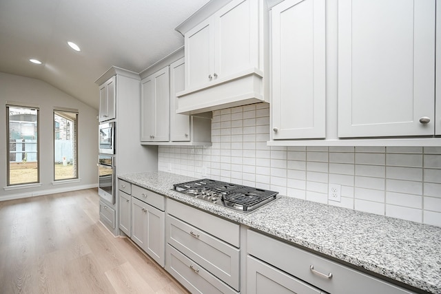 kitchen with appliances with stainless steel finishes, tasteful backsplash, lofted ceiling, light stone countertops, and light hardwood / wood-style flooring