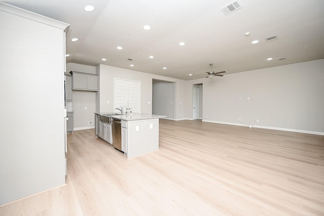 kitchen featuring sink, light wood-type flooring, stainless steel dishwasher, light stone countertops, and a kitchen island with sink