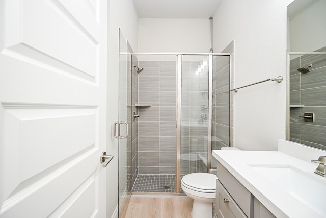 bathroom with wood-type flooring, toilet, a shower with shower door, and vanity