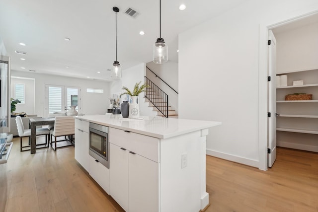 kitchen with a kitchen island, stainless steel microwave, decorative light fixtures, white cabinets, and light hardwood / wood-style flooring