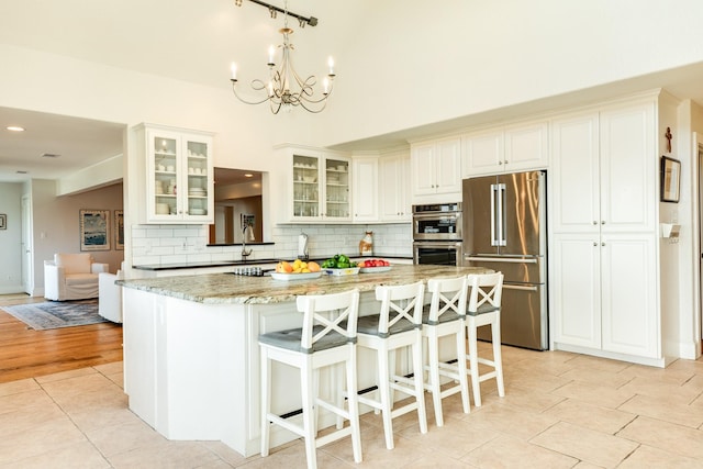 kitchen with appliances with stainless steel finishes, a kitchen island, light stone counters, tasteful backsplash, and a kitchen bar