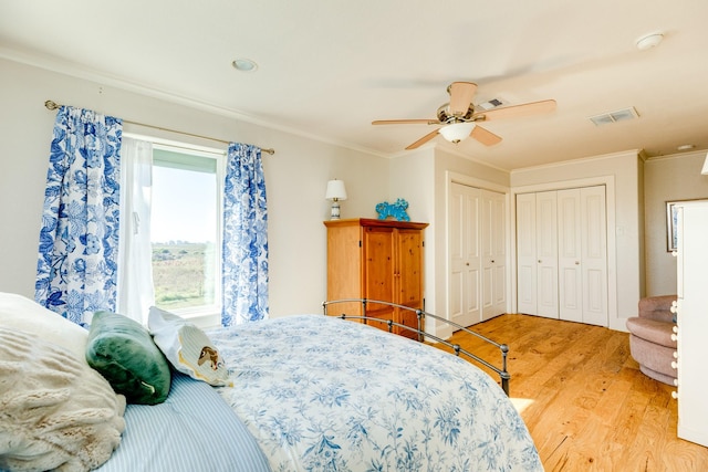 bedroom featuring ceiling fan, crown molding, multiple closets, and light wood-type flooring