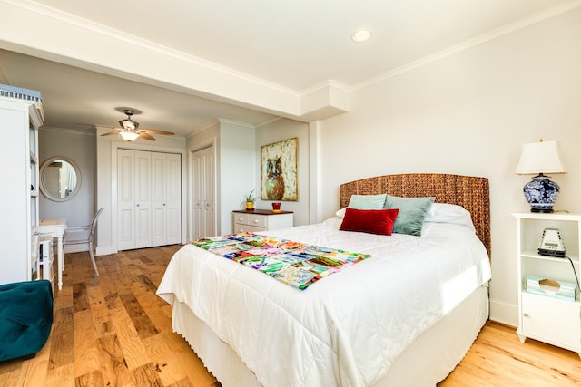 bedroom featuring multiple closets, crown molding, ceiling fan, and light wood-type flooring